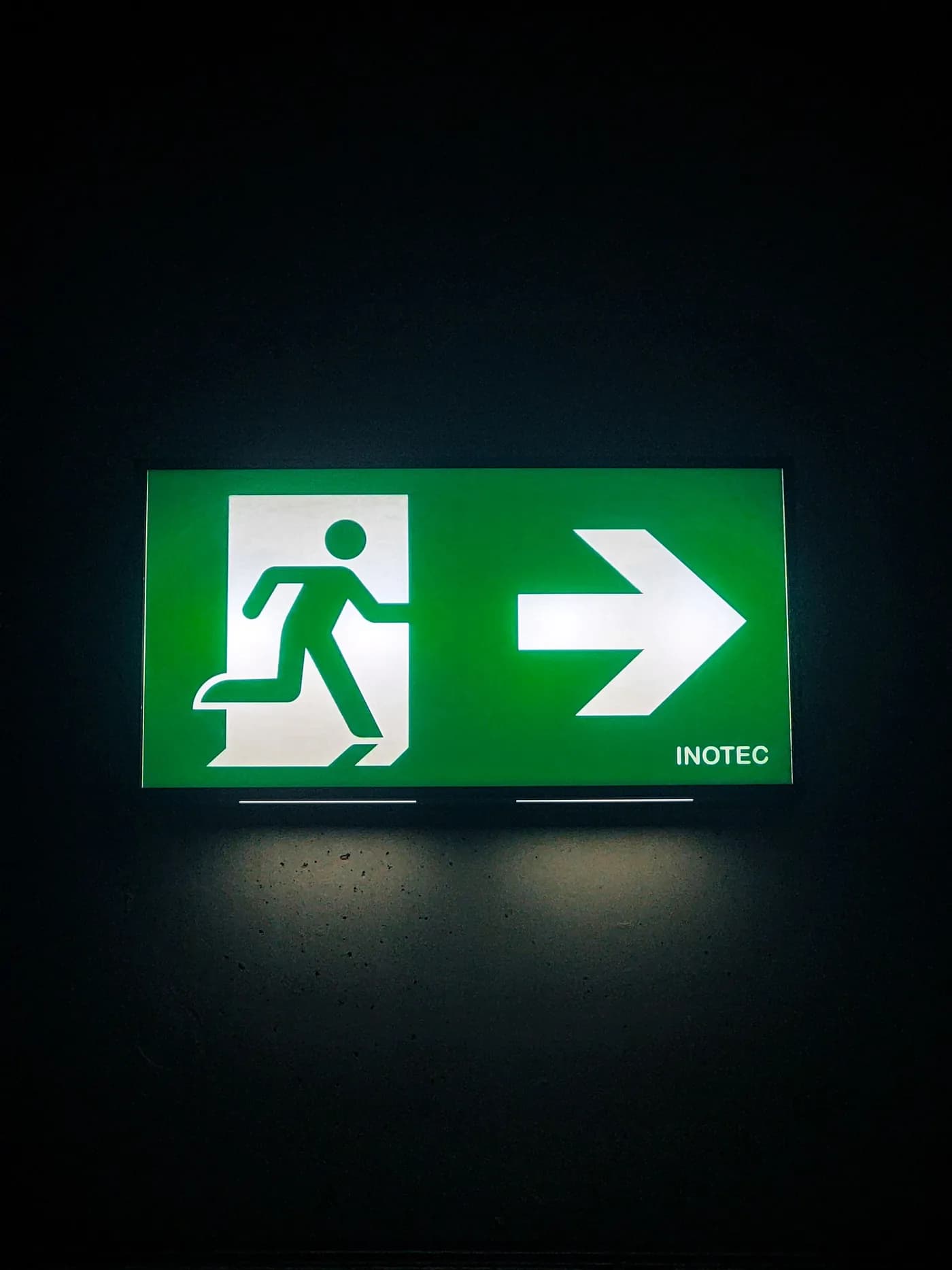 Señal de salida de emergencia iluminada en verde en un pasillo oscuro