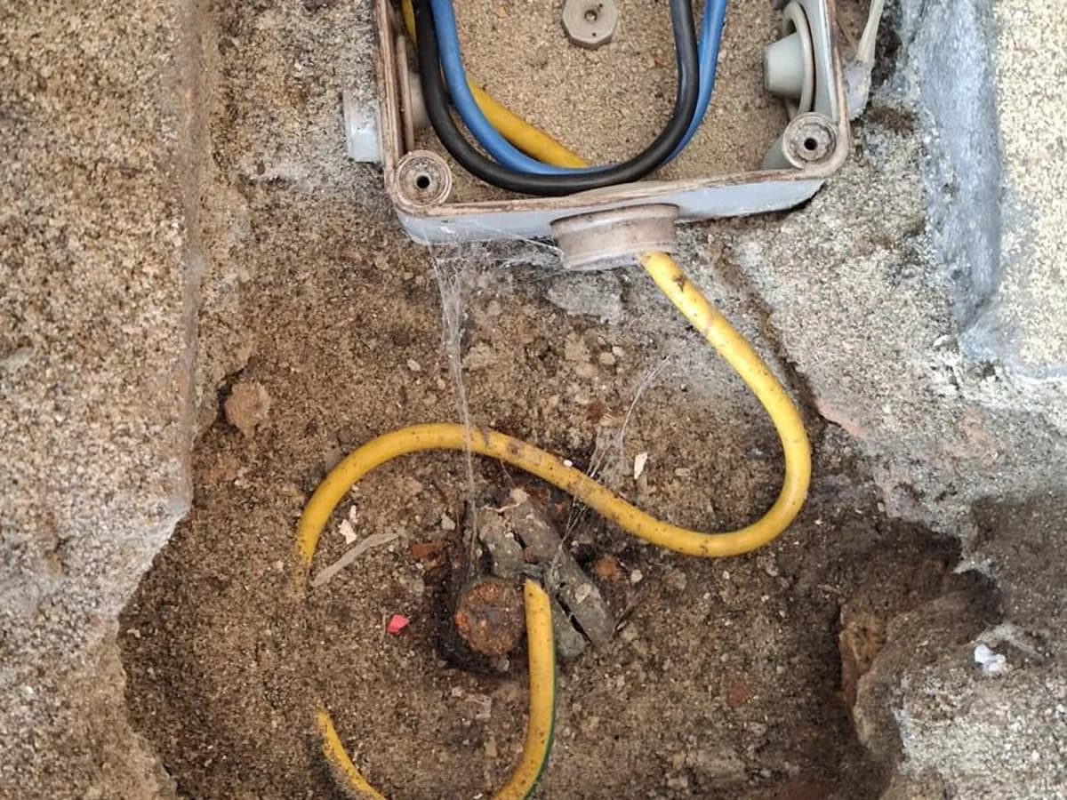 Caja de conexión eléctrica enterrada en el terreno con el conductor amarillo saliendo