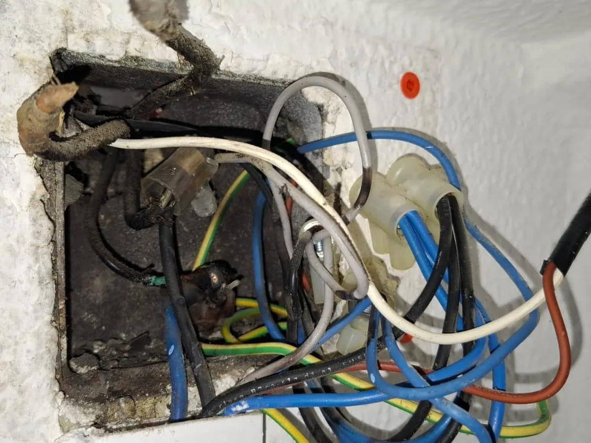 Caja de registro eléctrica abierta con los empalmes enmarañados y suciedad acumulada dentro del muro