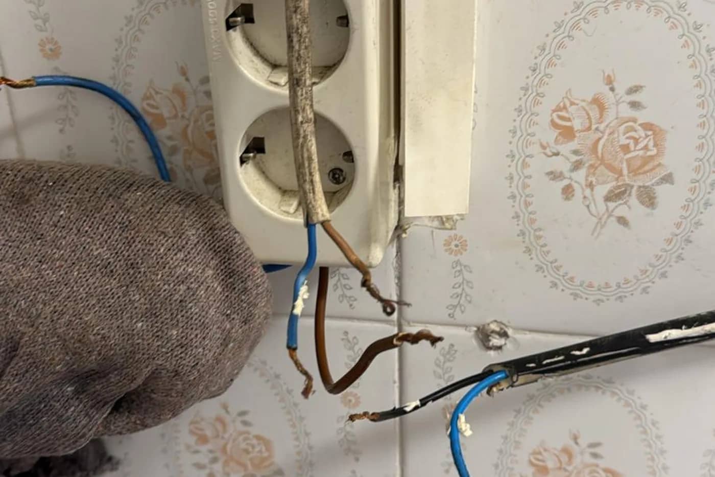 Enchufe de superficie antiguo sobre azulejo con el cableado original a la vista