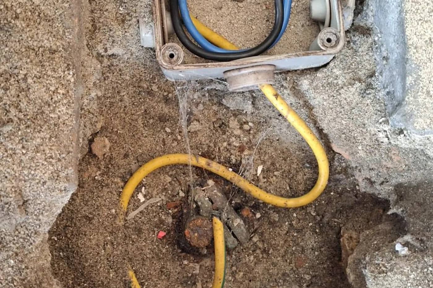 Caja de conexión eléctrica enterrada en el terreno con el conductor amarillo saliendo